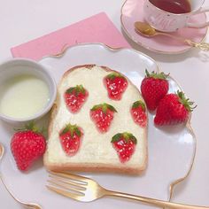 a piece of bread with strawberries on it and two cups of tea next to it