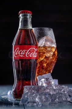 a bottle of coca - cola next to ice on a table with a glass full of coke