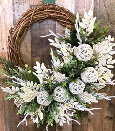 a wreath with white flowers and greenery hanging on a wooden wall