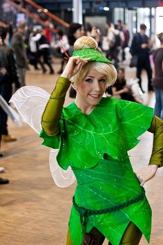 a woman dressed as tinkerbell standing on a wooden floor with people in the background