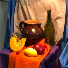 a table topped with vases and fruit on top of a purple cloth covered table