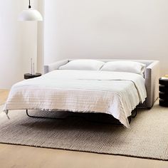 a white bed sitting on top of a wooden floor next to a lamp and table