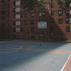 an empty basketball court in front of a large brick building with lots of windows and trees