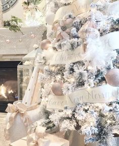 a white christmas tree with pink and silver ornaments in front of a fireplace mantel