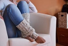 a woman sitting on top of a white couch next to a window with her legs crossed