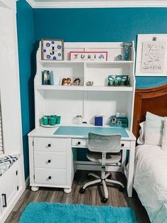 a white desk with a blue top and drawers in a bedroom next to a bed