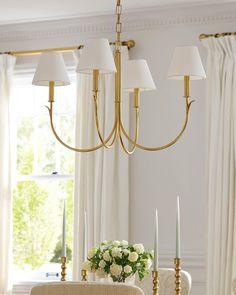 a chandelier hanging over a dining room table with white roses in the center