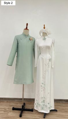 two dresses are on display in front of a white wall and wooden floor, one is light green