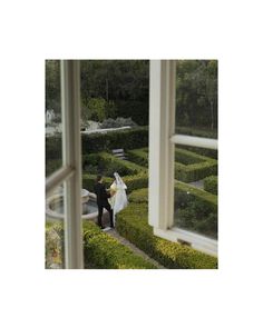 a bride and groom walking through a maze in the middle of a garden, looking at each other