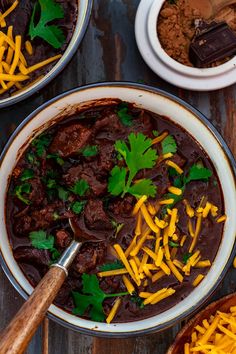 two bowls filled with chili and cheese on top of a wooden table next to other dishes