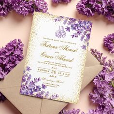 a wedding card with purple flowers and a brown envelope on a pink surface next to an envelope