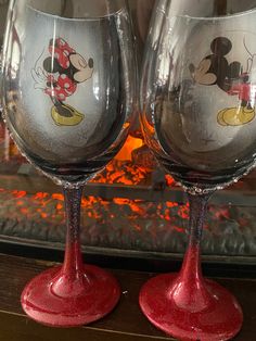 two wine glasses sitting next to each other on top of a wooden table in front of a fireplace