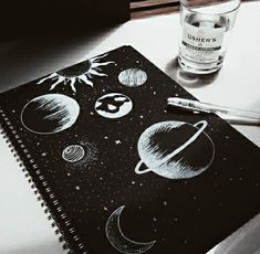 a notebook with drawings of planets and the sun on it next to a glass of water