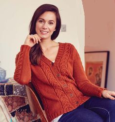 a woman sitting in a chair wearing an orange cabled cardigan sweater and jeans