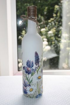 a glass bottle with flowers painted on it sitting in front of a window sill