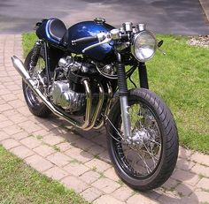 a blue motorcycle parked on the side of a brick road next to grass and trees