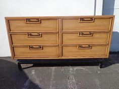 a wooden dresser sitting on top of a sidewalk next to a white wall and cement floor