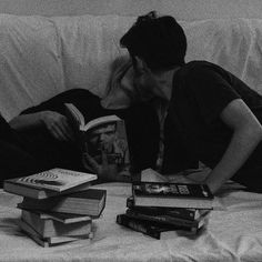 a man and woman kissing while laying on a couch with books stacked on top of them