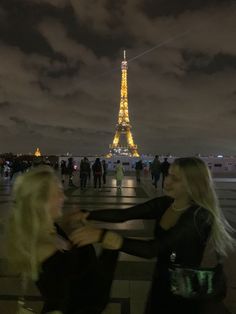 two women standing next to each other in front of the eiffel tower at night