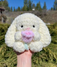 a hand holding a crocheted white stuffed animal with a pink flower in it's mouth