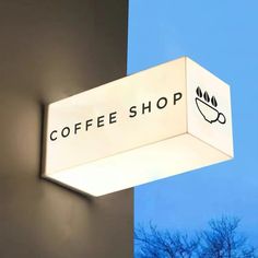 a coffee shop sign hanging from the side of a building with trees in the background