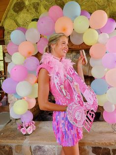 a woman in a pink dress holding a can and standing next to a bunch of balloons