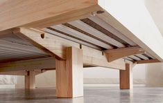 the underside of a wooden bed frame in a room with concrete flooring and white walls