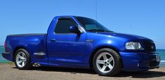 a blue pick up truck parked on the side of the road near the ocean and sand