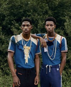 two young men standing next to each other in front of some trees and bushes with beads on their neck