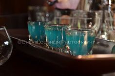 there are many glasses on the tray and one is filled with blue liquid in it