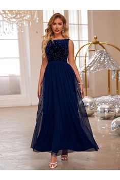 a woman in a long blue dress standing next to a chandelier and christmas decorations