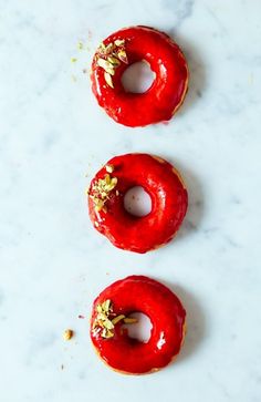 three donuts with red glaze and sprinkles on them sitting on a white surface