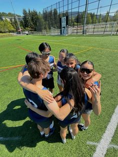 a group of young women standing on top of a soccer field hugging eachother