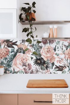 a kitchen counter with flowers on the wall and shelves above it, along with a wooden cutting board