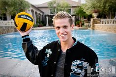 a young man holding a yellow and black ball in front of a swimming pool,