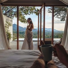 a woman standing in front of a bed holding a cup