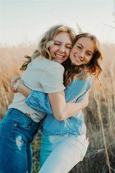 two young women hugging each other in the middle of a field with tall grass behind them