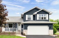 a blue house with white trim and two car garages in the front yard on a sunny day