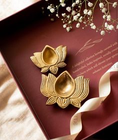 two golden flower shaped dishes sitting on top of a red box next to white flowers