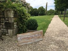 a wooden sign sitting on top of a gravel road next to a lush green field