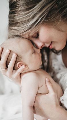 a woman holding a baby in her arms and kissing it's face with both hands