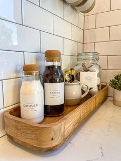 some jars are sitting on a wooden tray in the middle of a white tiled kitchen