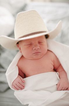 a baby wrapped in a blanket with a cowboy hat on it's head and eyes closed