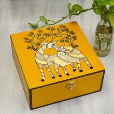 a yellow box sitting next to a vase filled with flowers and greenery on top of a table