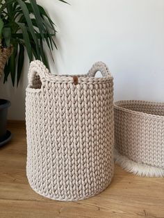 two knitted baskets sitting on top of a wooden floor next to a potted plant