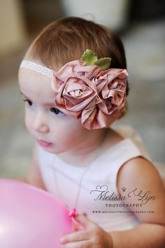 a baby girl with a flower in her hair holding a balloon and wearing a headband