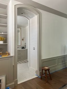 an empty room with white walls and wood flooring in the foreground is a wooden stool