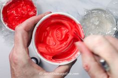 two hands are painting the inside of a white bowl with red food coloring on it