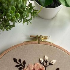 a potted plant sitting on top of a table next to a cross stitch embroidery