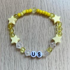 a yellow beaded bracelet with white stars and the word us on it, sitting on top of a wooden table